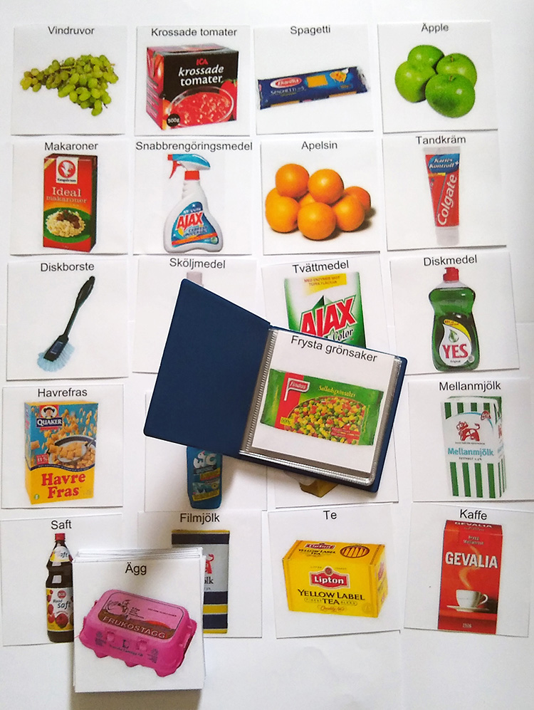 En liten bok med plastfickor ligger ovanpå flera inplastade småbilder av mat och hushållsartiklar. 